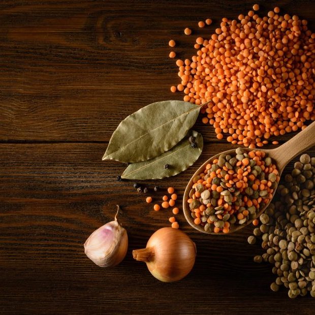 Red and green Lentils with onion, garlic and spices with wooden spoon on wooden background. Healthy lifestyle. Lentil soup ingredients . Flat lay. Top view. Copy space for text.