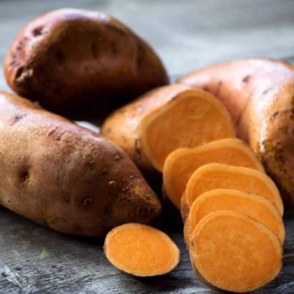 Raw sweet potatoes on wooden background Raw onions